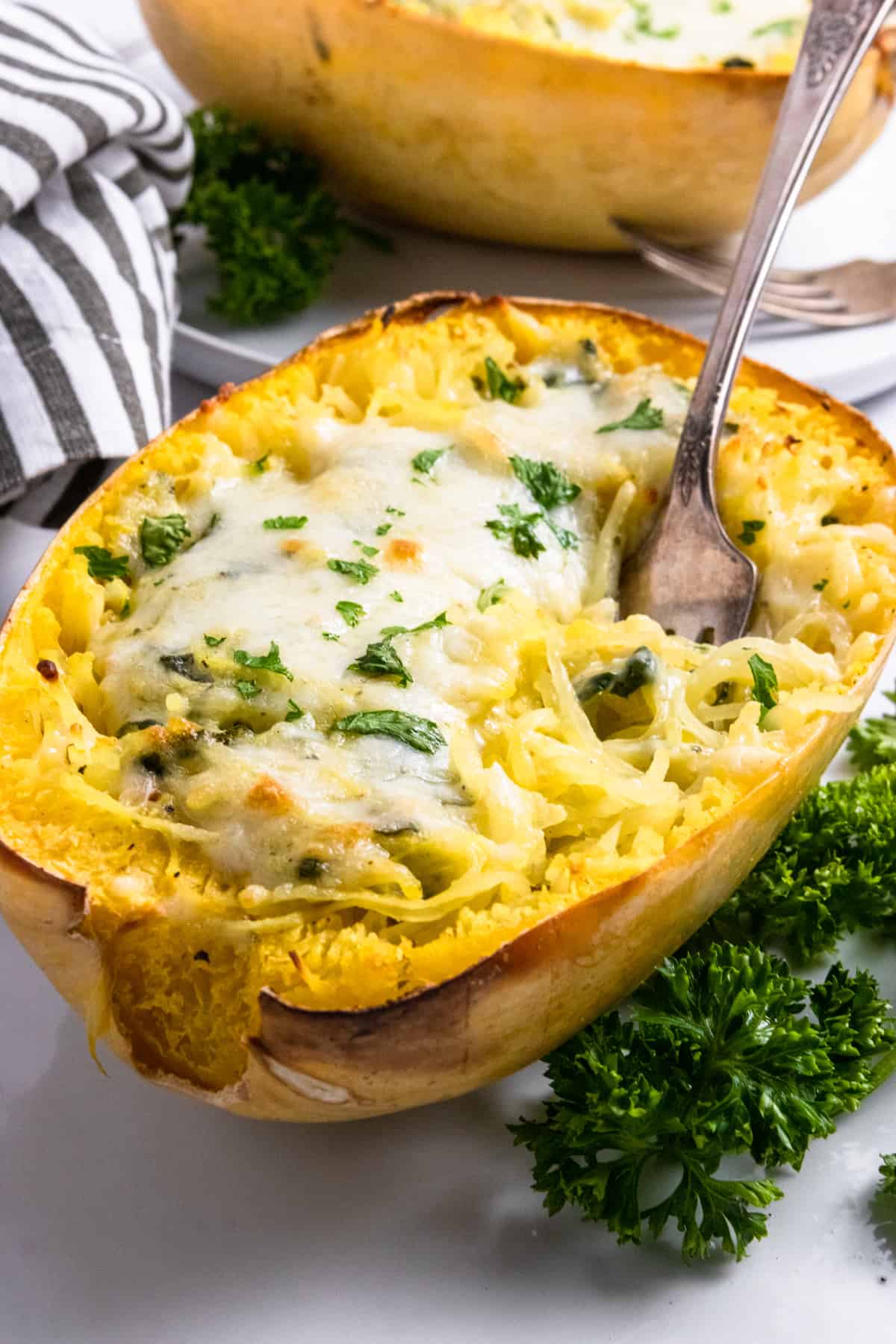 Spaghetti squash with cheese and pesto baked on top with spoon.