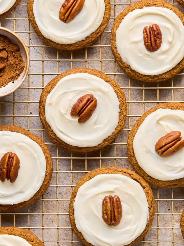 Iced molasses cookies with pecan half on top arranged on cooling rack.