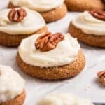 Pumpkin spice cookies iced with cream cheese maple icing and pecan halves on top of each.