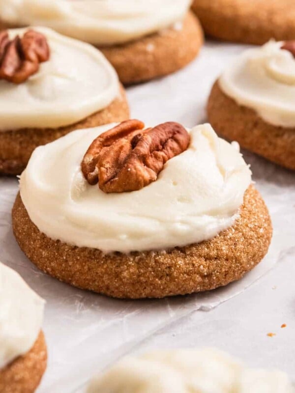 Pumpkin spice cookies iced with cream cheese maple icing and pecan halves on top of each.