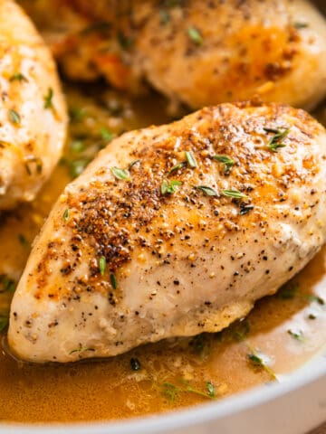 Seared chicken breast in skillet in buttery white wine sauce.