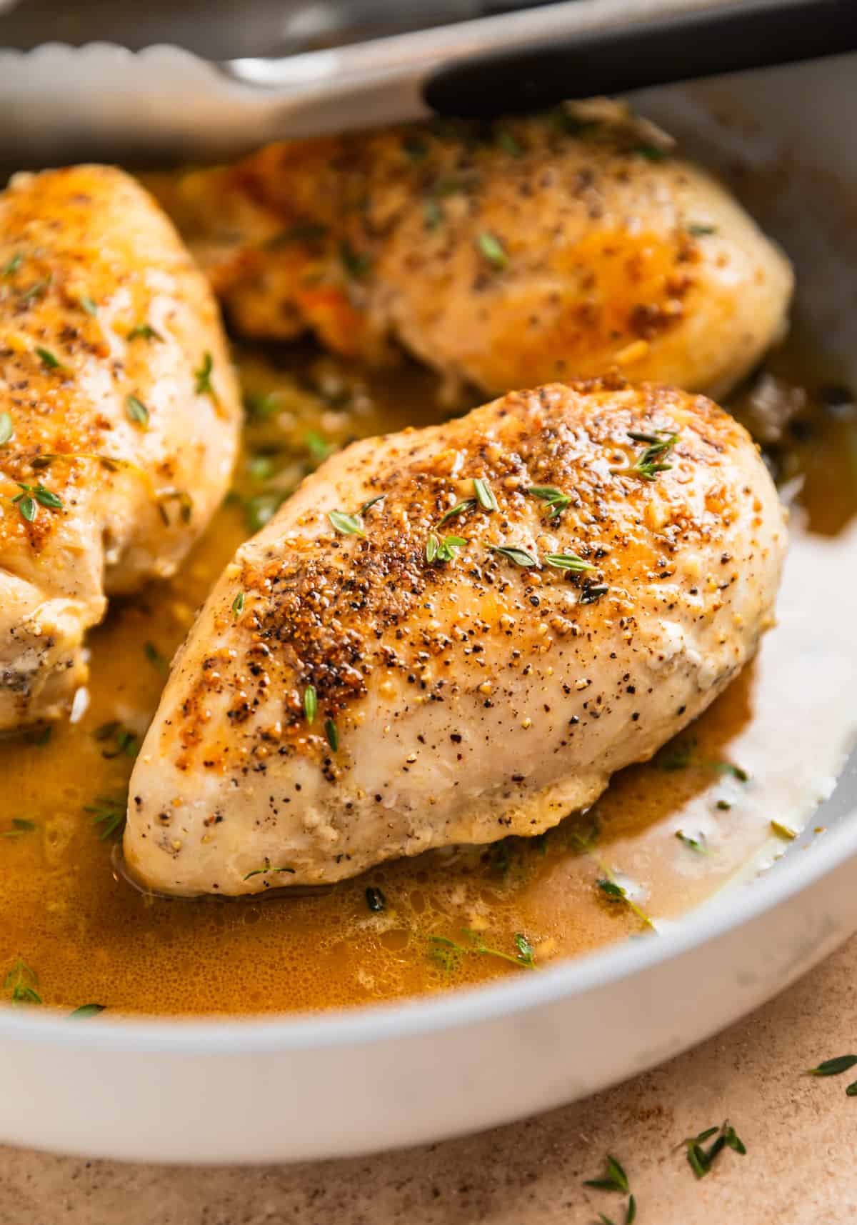 White wine chicken breasts in skillet topped with pepper and fresh thyme.