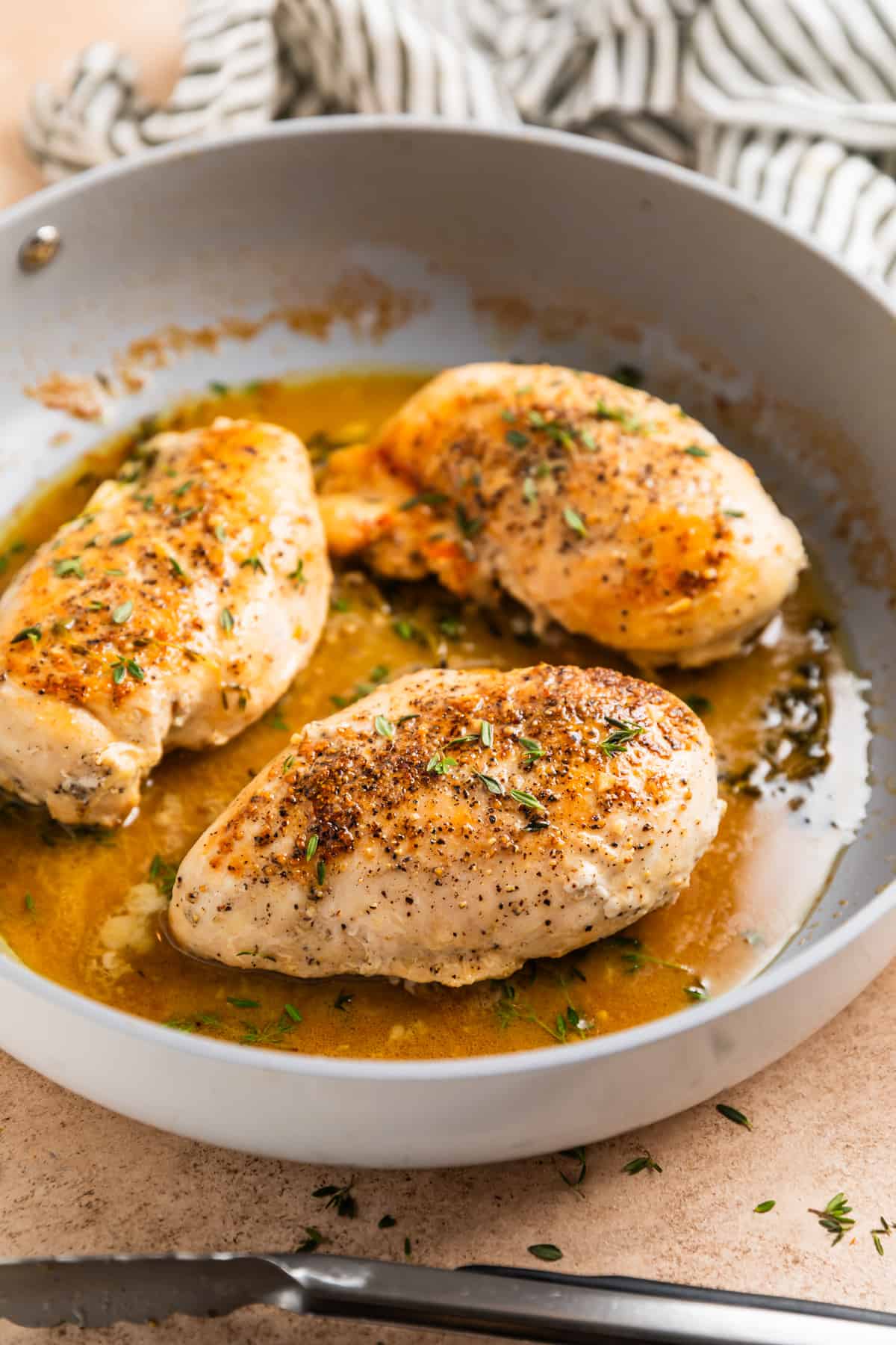 Cooked chicken breasts in skillet with white wine sauce with thyme sprigs.