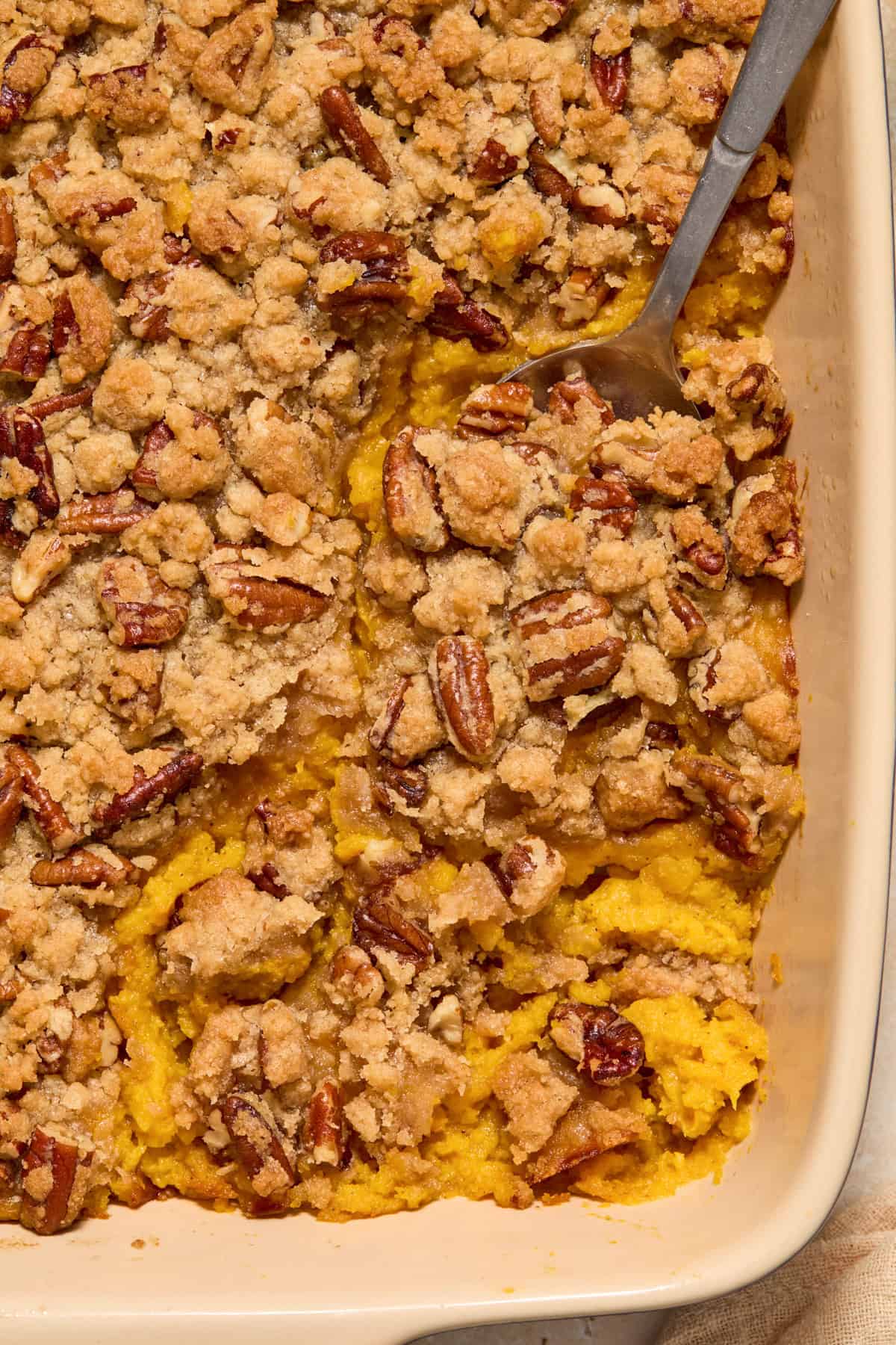 Serving spoon scooping into pecan crumble topped squash mixture in baking pan.