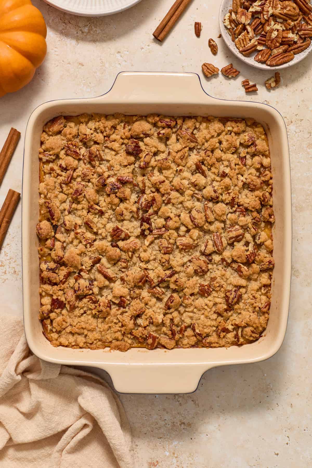 Baked crumble topped squash casserole with linen, pumpkin, cinnamon stick and other ingredients surrounding.