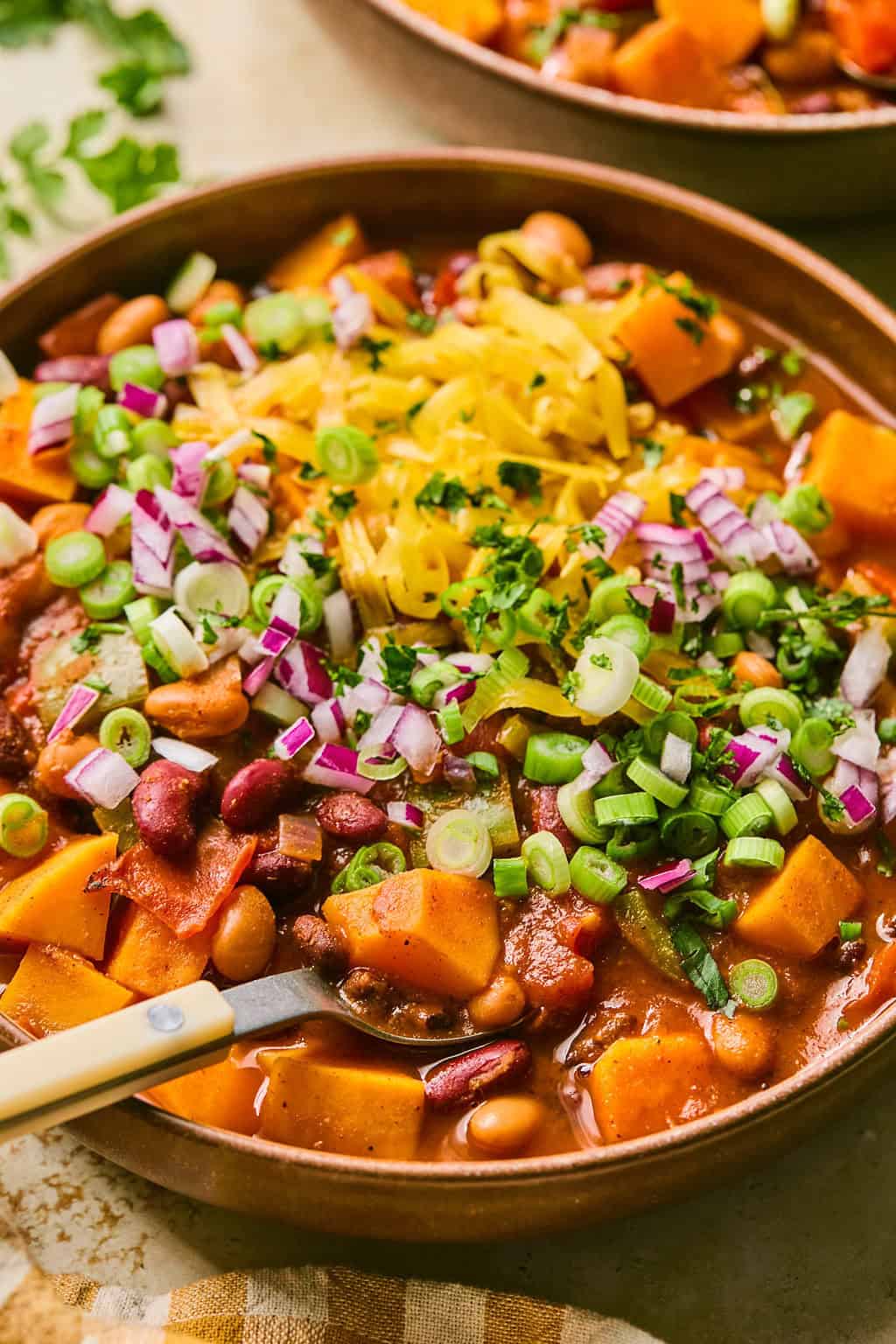 Bowl with spoon scooping into butternut squash chili topped with shredded cheese and onions.