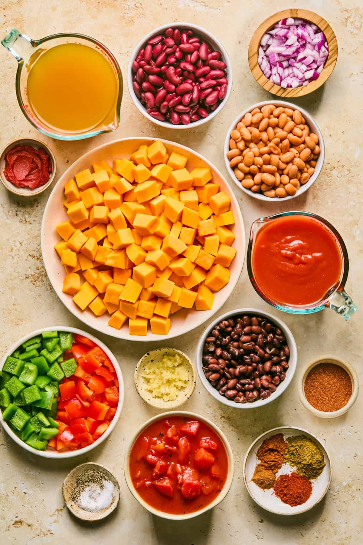 Beans, broth, cubed butternut squash, peppers and other ingredients on surface.