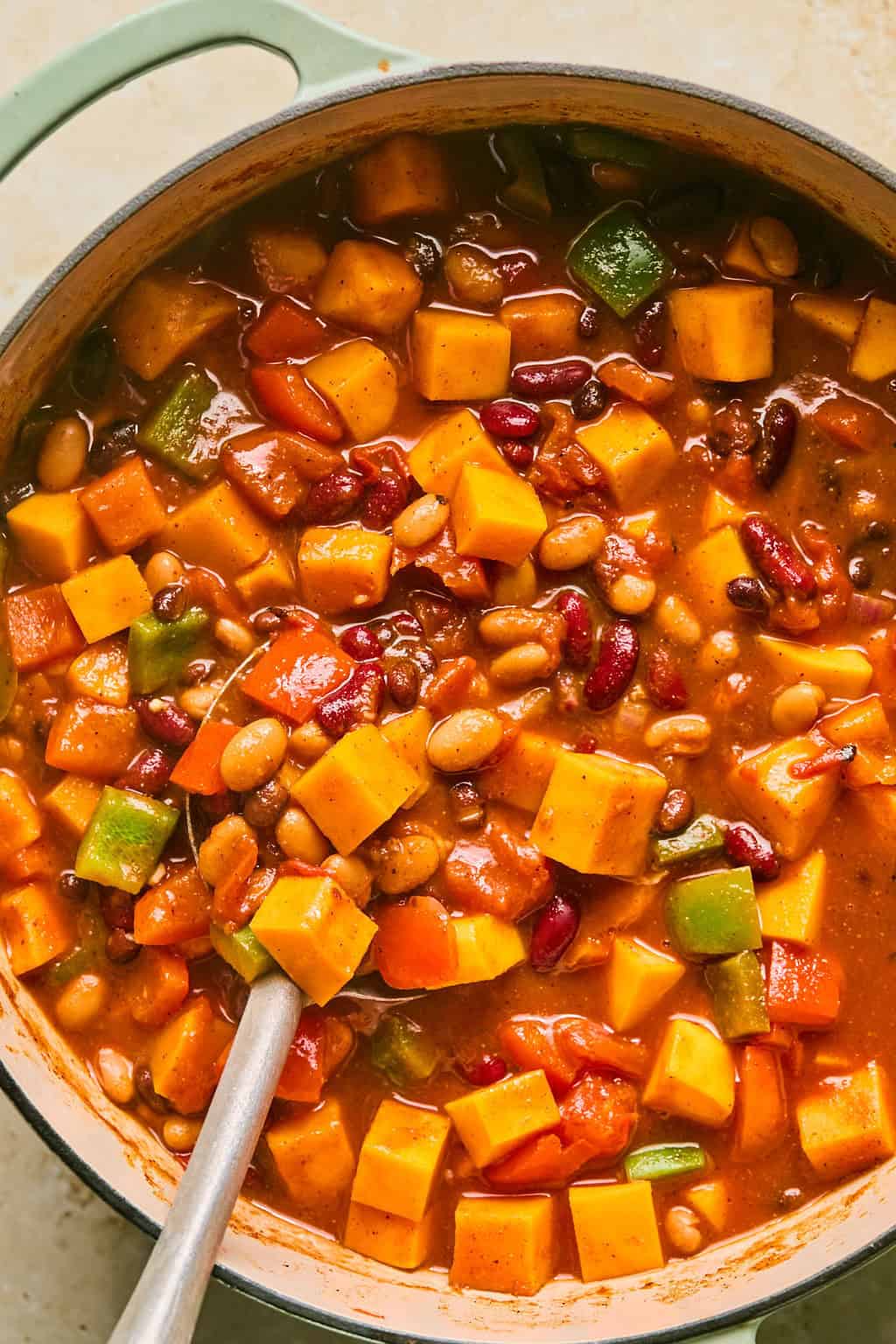 Cooked butternut squash chili in pot with spoon scooping into it.