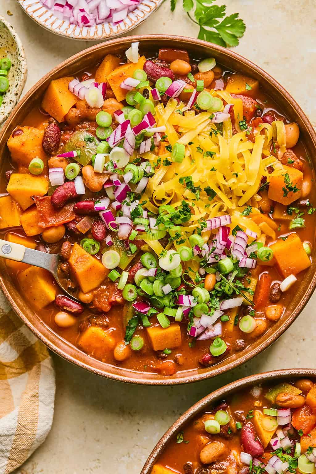 Bowl of butternut squash chili with cheese, onion and cilantro garnish on top.