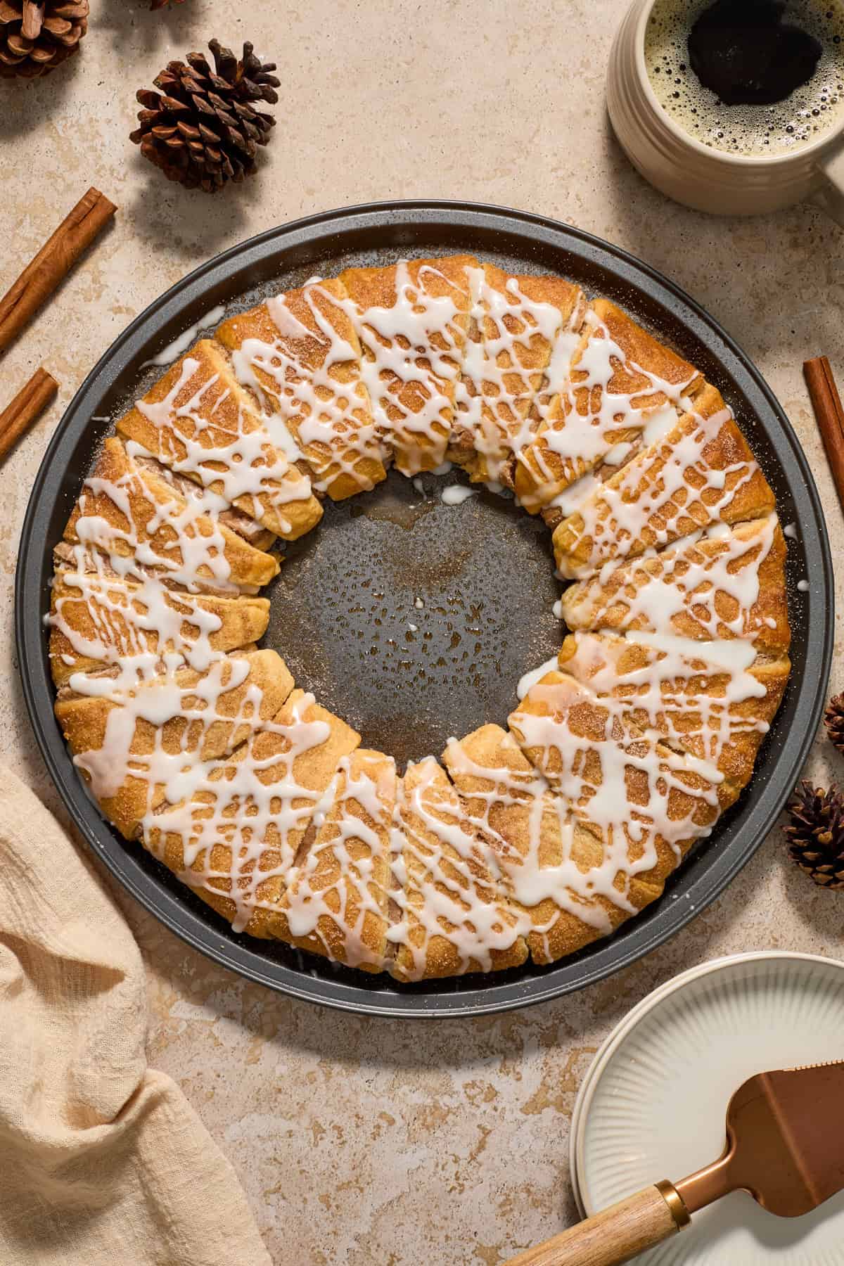 Cinnamon crescent roll wreath on pan with coffee and cinnamon sticks surrounding.