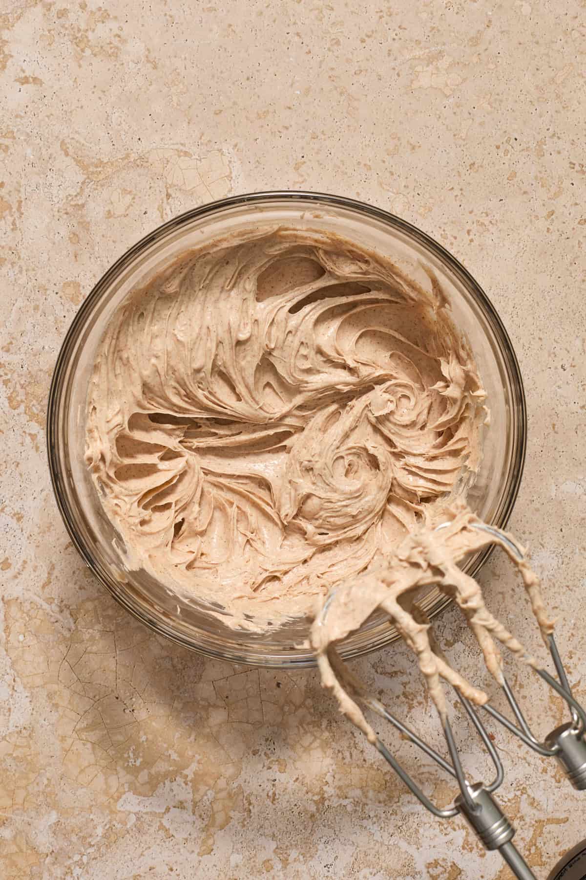 Creamed cream cheese and sugar in bowl with electric mixer propped to the side.