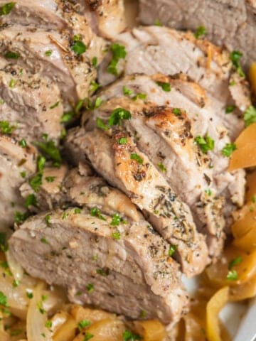 Pork tenderloin with apples sliced and topped with parsley.