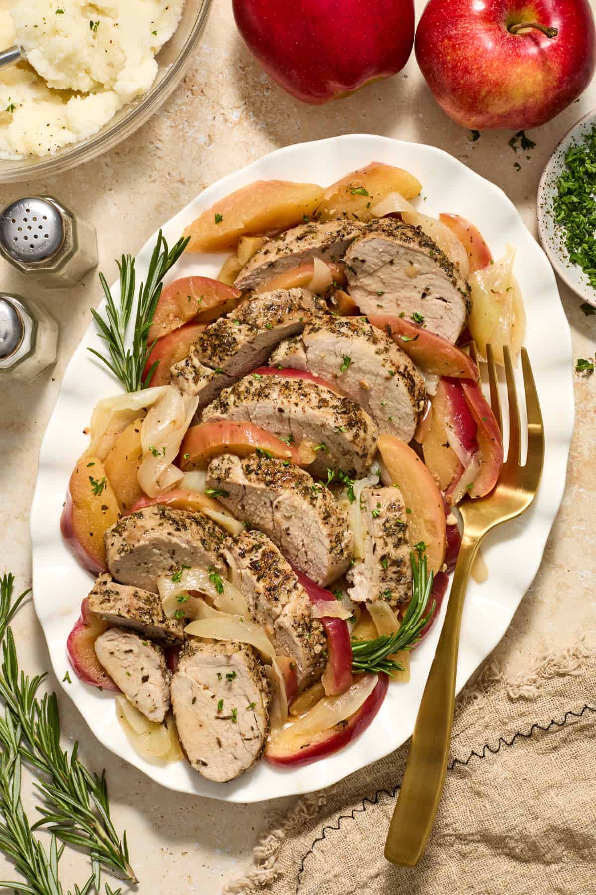 Serving platter with pork tenderloin slices, apples and rosemary.