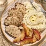 Pork tenderloin sliced on plate with apples and mashed potatoes.