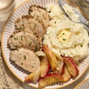 Pork tenderloin sliced on plate with apples and mashed potatoes.