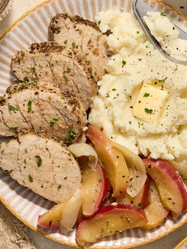 Pork tenderloin sliced on plate with apples and mashed potatoes.