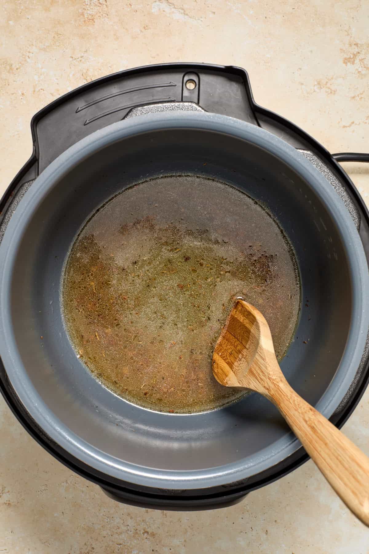 Deglazed instant pot with broth and wooden spoon.
