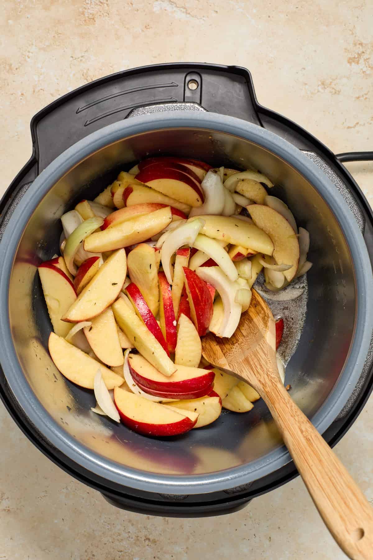 Apples, onion, butter and brown sugar added to pot with wooden spoon.