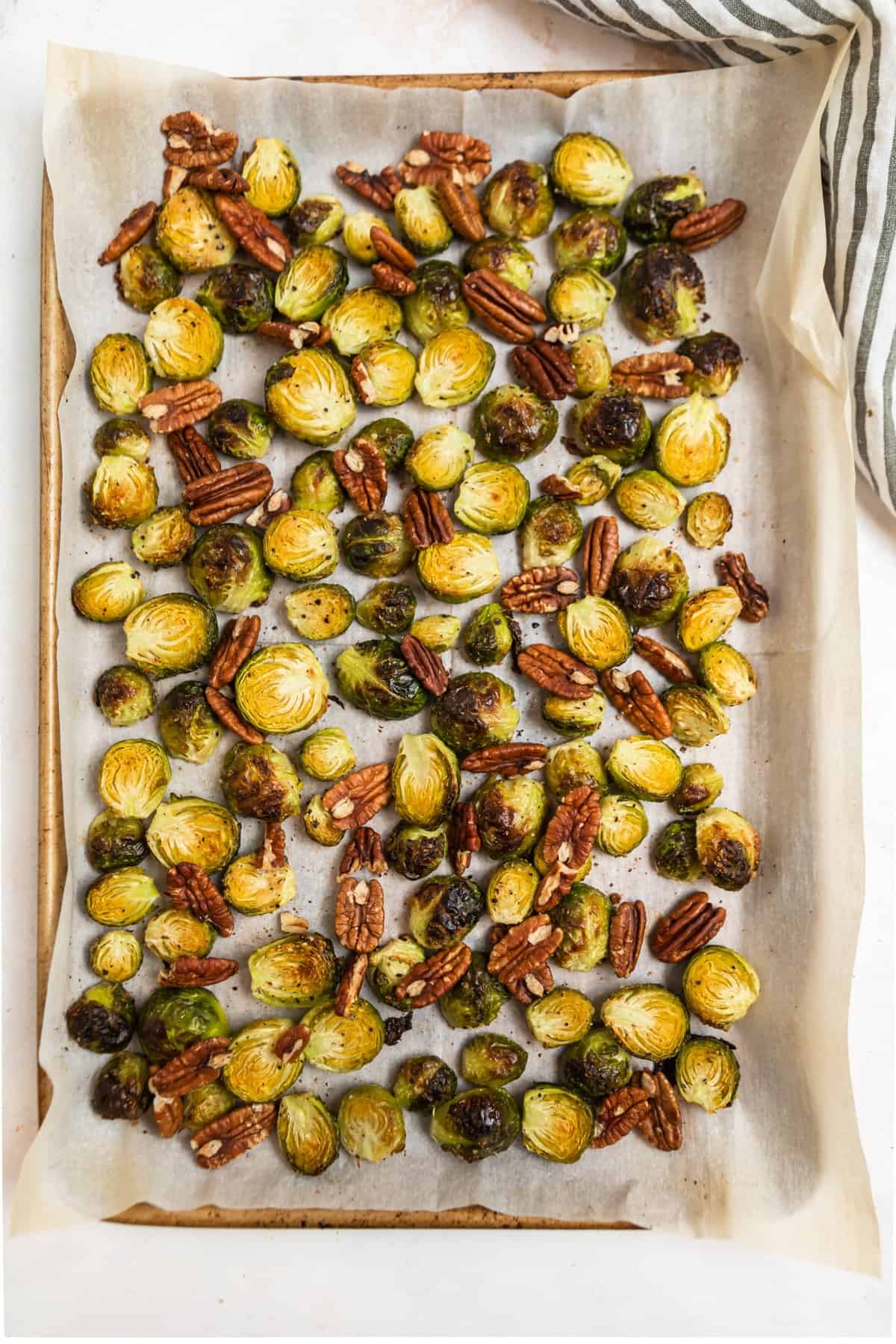 Sheet pan lined with parchment with roasted Brussels sprouts and pecans.