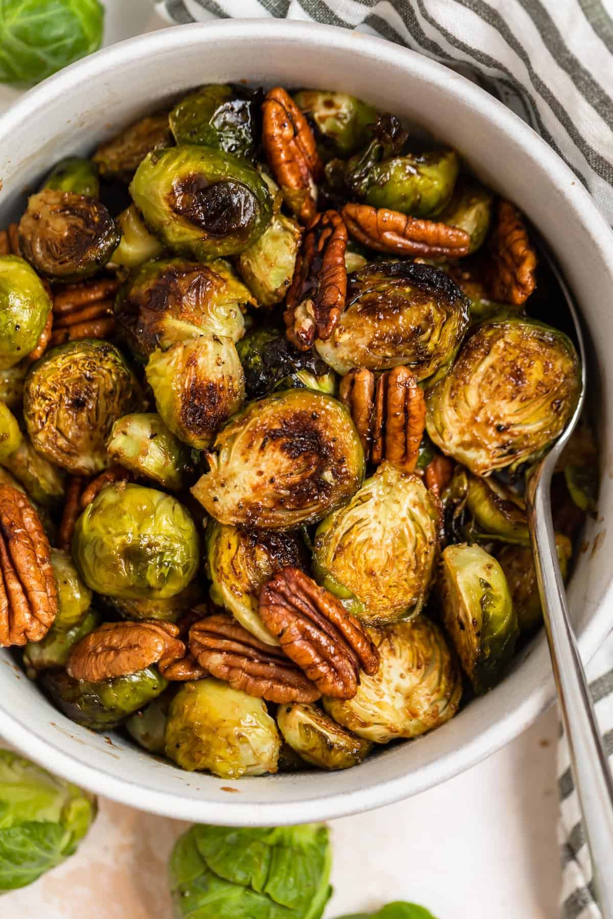 Serving bowl with roasted maple balsamic brussels sprouts and spoon.