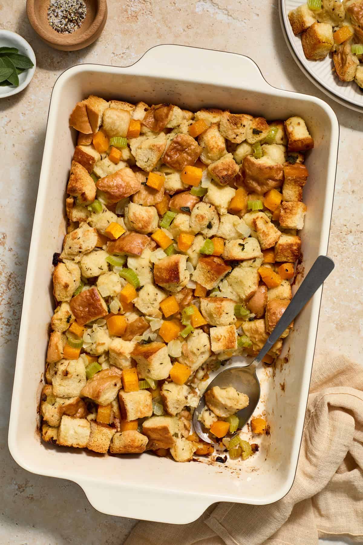 Baking pan with baked butternut squash stuffing with spoon scooping into the dish.