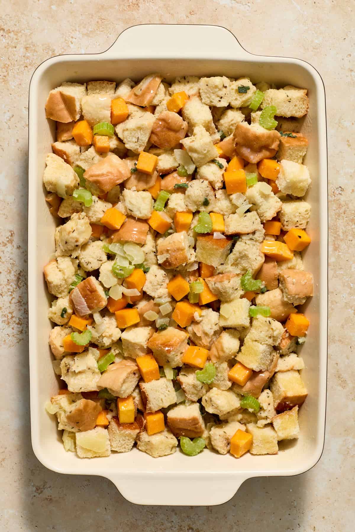 Baking pan with stuffing ingredients before baking with melted butter drizzled over top.