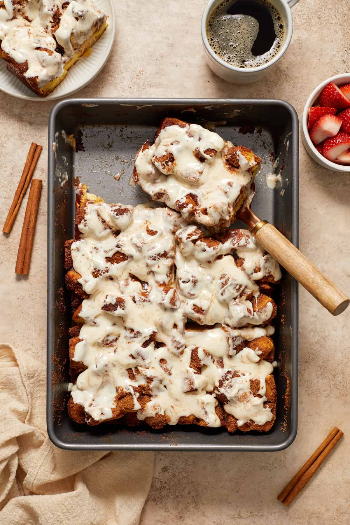 Slice of baked French toast casserole topped with cream cheese frosting set aside in baking pan.