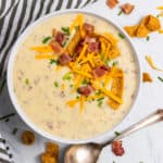 Potato soup in white bowl with toppings.