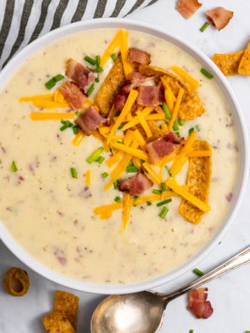 Potato soup in white bowl with toppings.