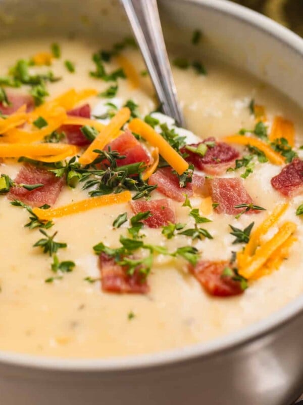 Beige bowl with potato soup topped with bacon, cheese, chives and sour cream.