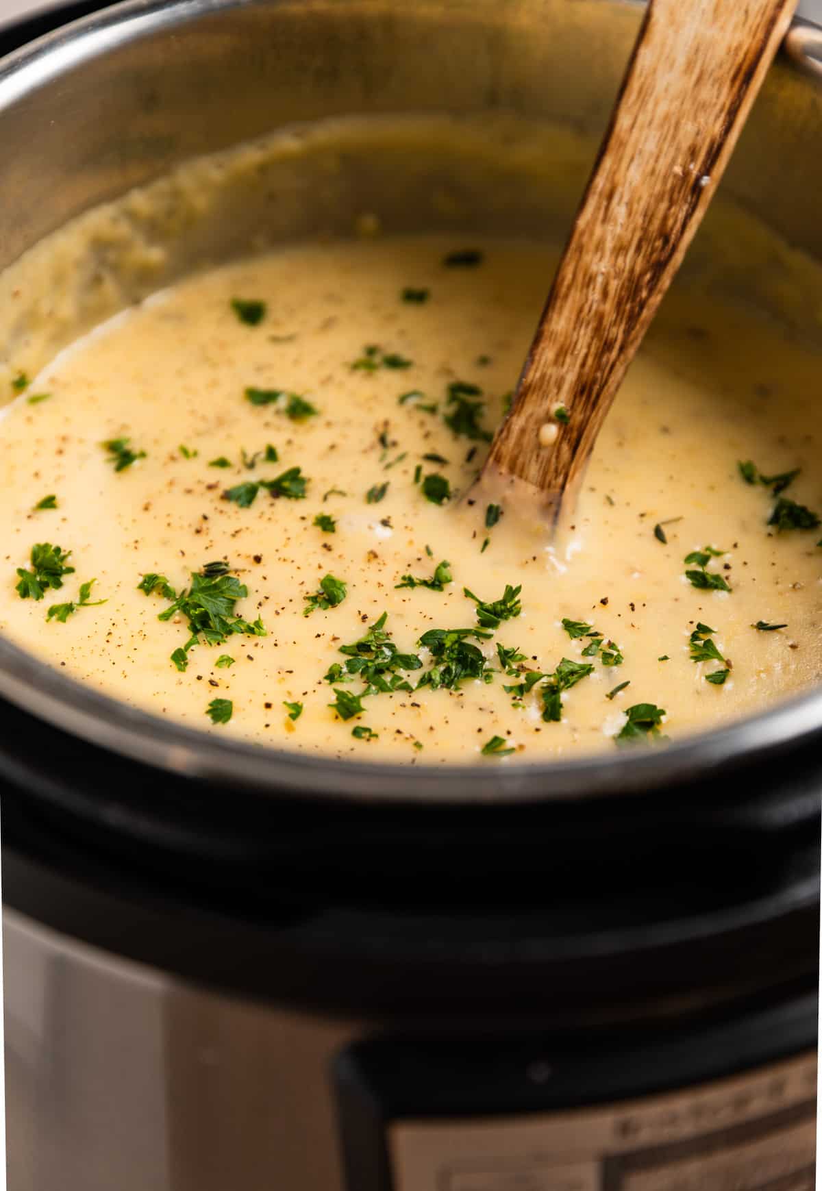 Instant pot with soup topped with chopped parsley and wooden spoon inserted.