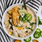 Creamy white chicken chili with cream cheese in bowl with jalapeño, fritos and cheese.