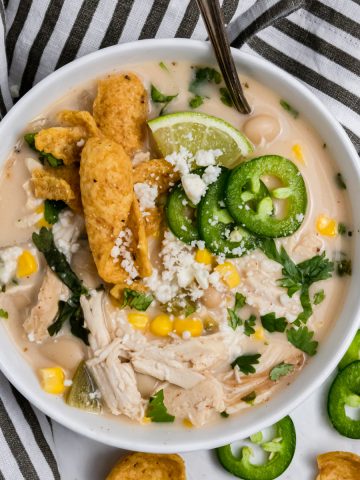 Creamy white chicken chili with cream cheese in bowl with jalapeño, fritos and cheese.
