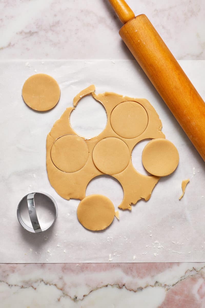 Rolled shortbread cookie dough on parchment with cookie cutter and rolling pin.