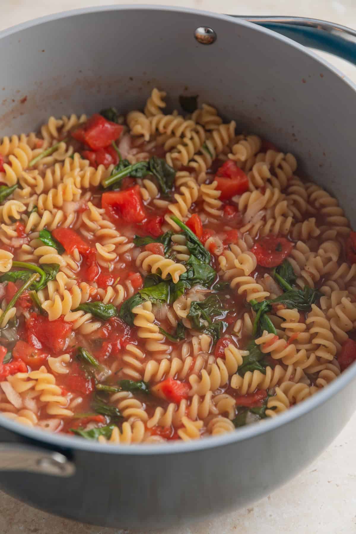Boiled pasta with spinach and tomatoes in pot.