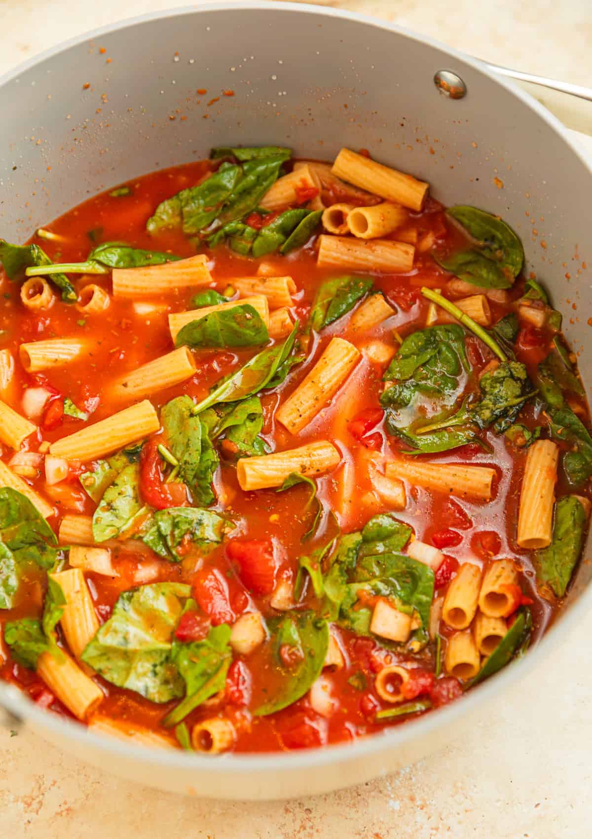 Pot with pasta, broth, spinach, and tomatoes.