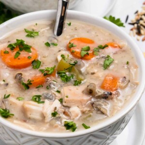Creamy crockpot chicken rice soup in bowl with spoon and fresh parsley.