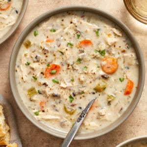 Creamy crockpot chicken wild rice soup in bowl with spoon and chopped parsley on top.