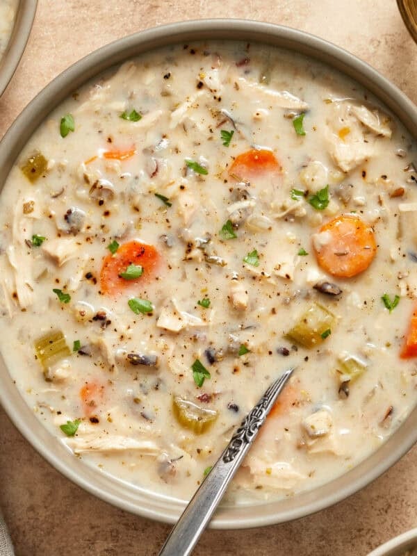 Creamy crockpot chicken wild rice soup in bowl with spoon and chopped parsley on top.