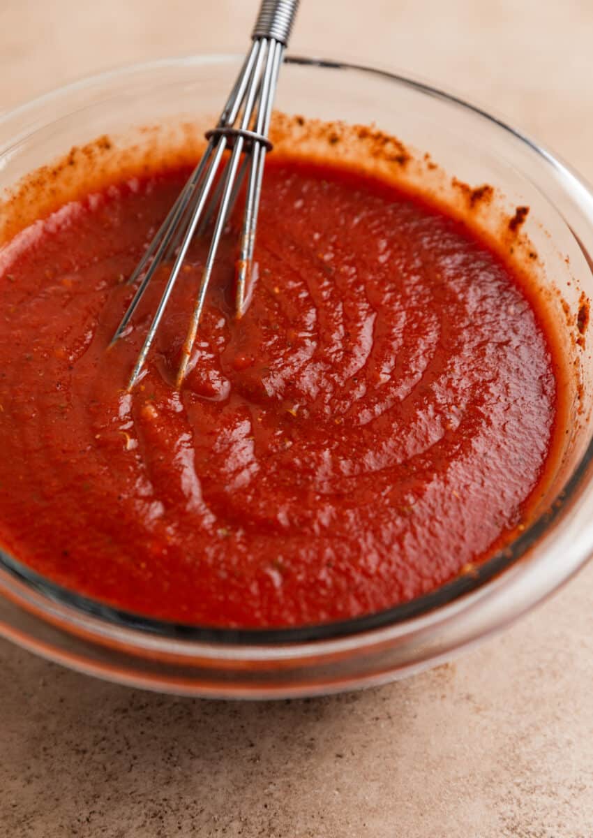Enchilada sauce in glass bowl with whisk.