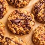Oatmeal cookies with peanut butter and banana on parchment paper with chocolate drizzle over top.