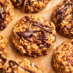 Oatmeal cookies with peanut butter and banana on parchment paper with chocolate drizzle over top.