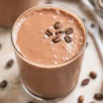 Peanut butter coffee smoothie in glass with coffee beans on top.