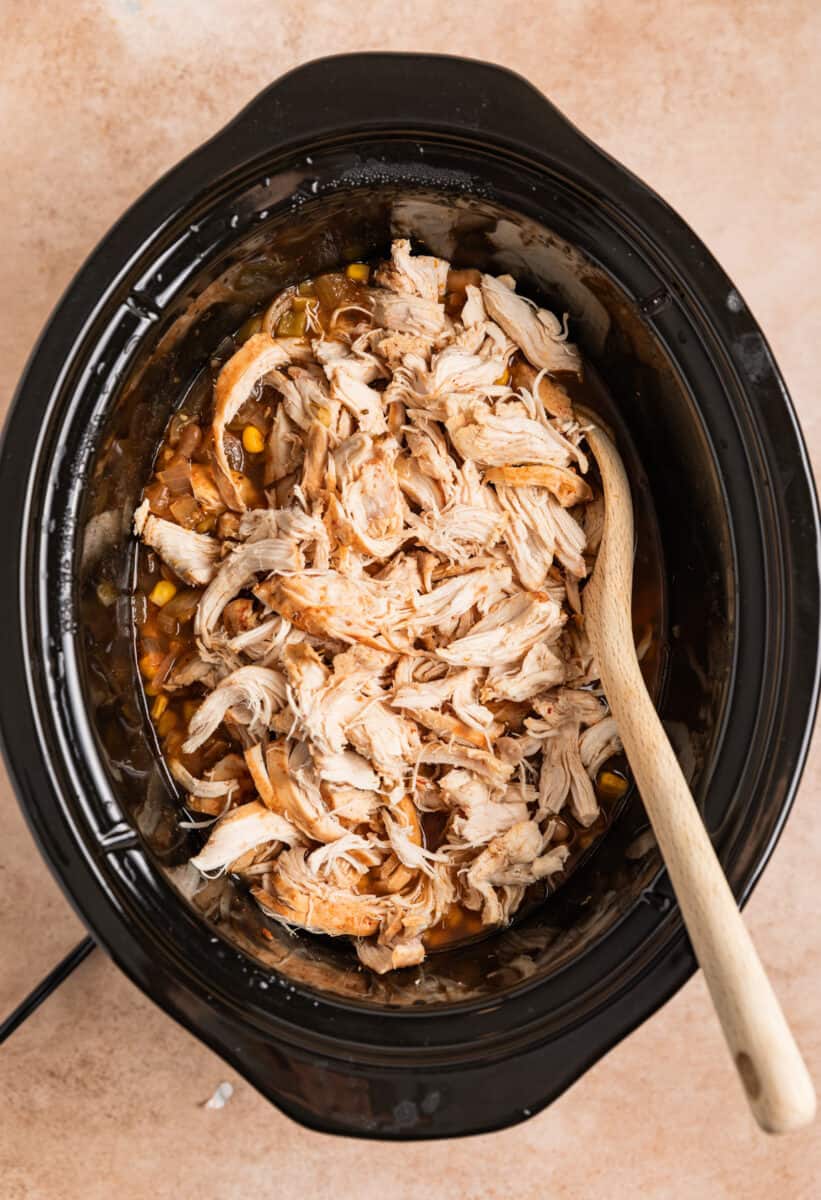 Chicken added to chili cooking in crockpot with wood spoon