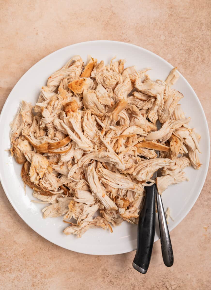 Chicken shredded on plate with knife and fork.