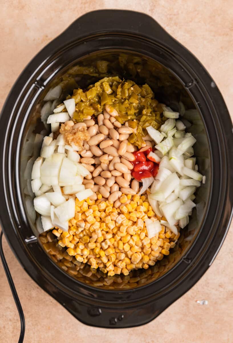 Corn, onion, green chiles, garlic and sriracha covering chicken in crockpot.