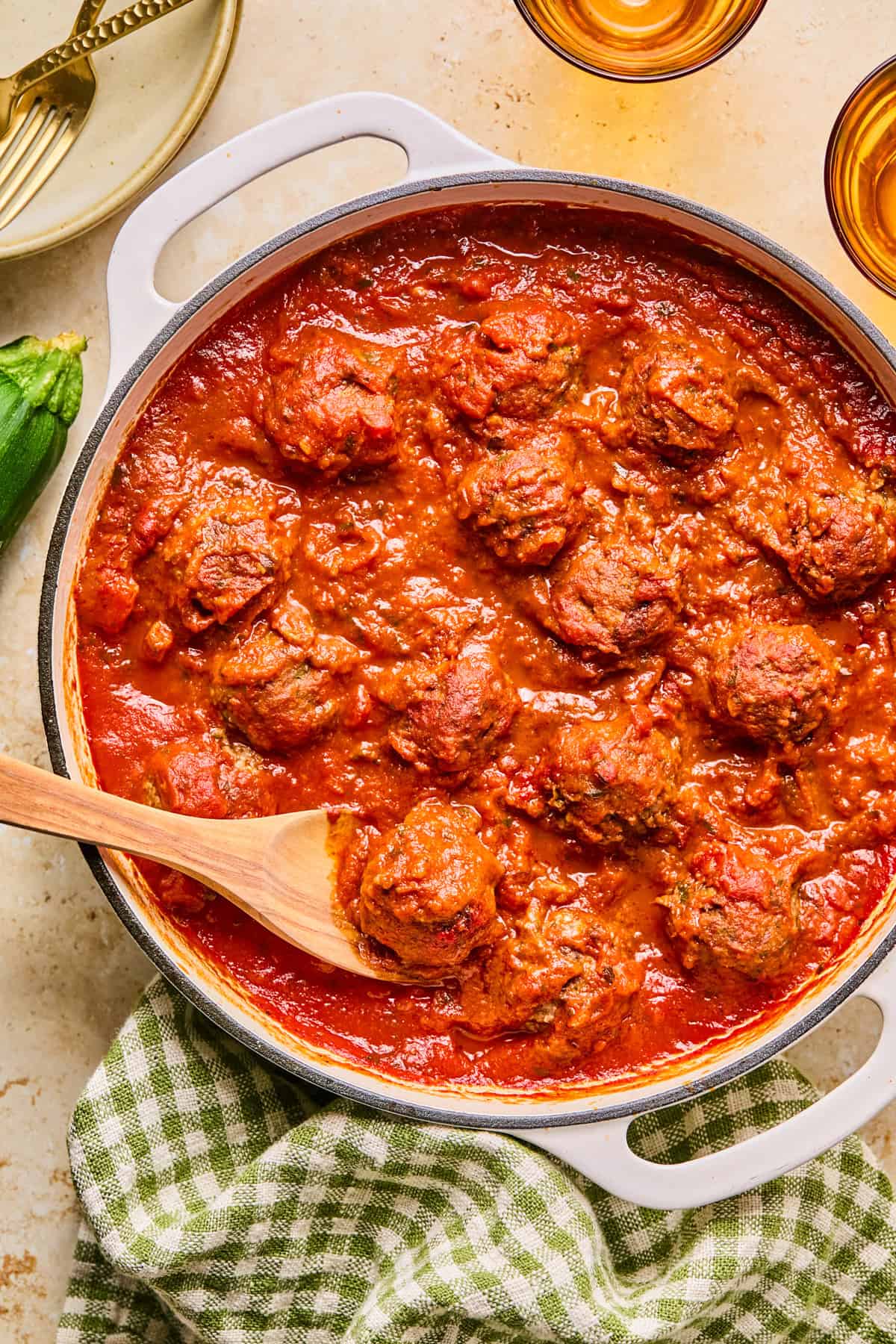 Beef and zucchini meatballs in pot with marinara and wooden spoon.
