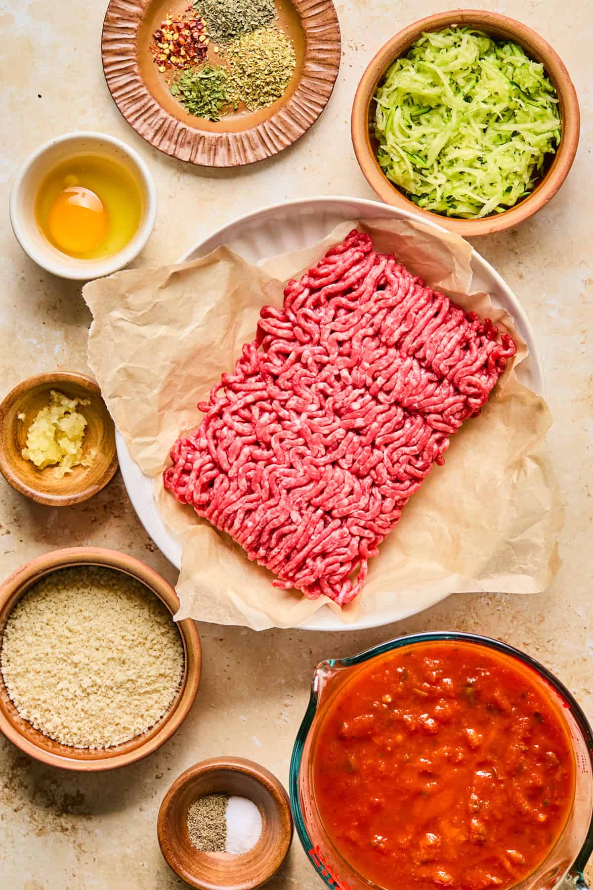 Ground beef, marinara, shredded zucchini and other ingredients on surface.