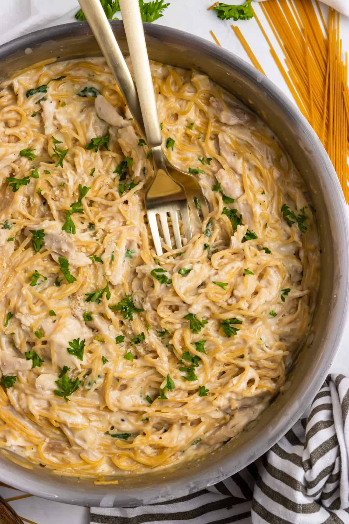 Chicken Alfredo in pan with fresh parsley and forks in pasta.