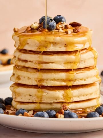 Stack of super fluffy pancakes on plate with blueberries, pecans, and maple syrup.